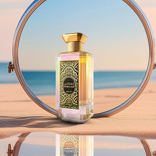 Zimaya Inekas Solis Perfume bottle with decorative label on a reflective surface with sunglasses and beach background