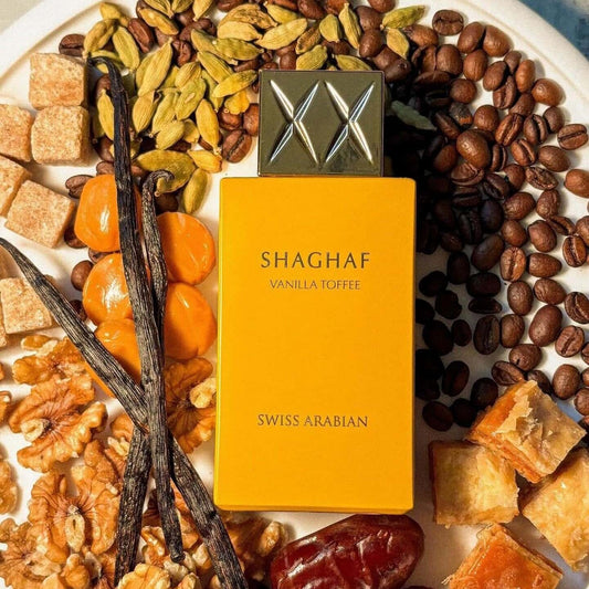 Shaghaf Vanilla Toffee perfume bottle surrounded by vanilla beans, coffee beans, and dried fruits on a white plate.