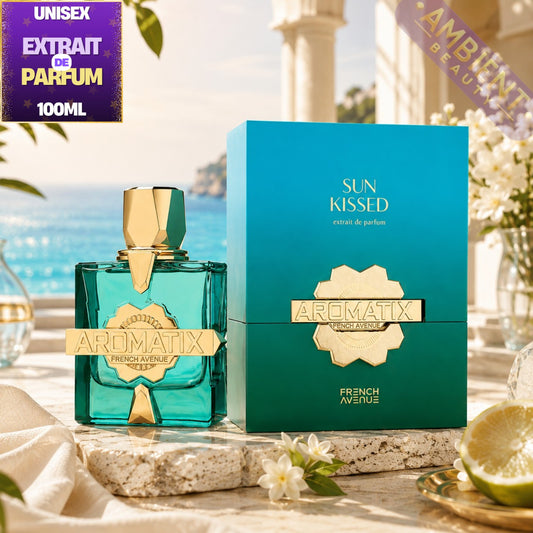 Aromatix 'French Avenue Sun Kissed' unisex extrait de parfum 100ml bottle in a turquoise glass with gold accents, displayed next to its teal and gold packaging box on a stone surface with a beach background.