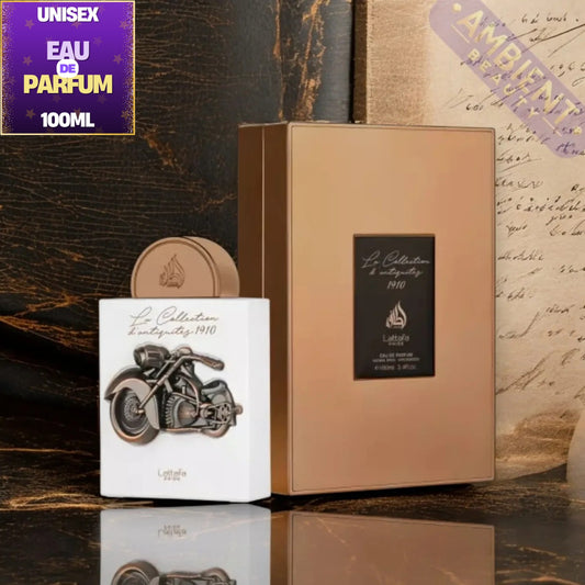 A perfume product display showing a tall metallic rose-gold box, a white box with a motorcycle illustration, and a round matching cap, set against a dark wood and vintage script background. A purple 'EAU DE PARFUM 100ML' label appears in the top-left corner.