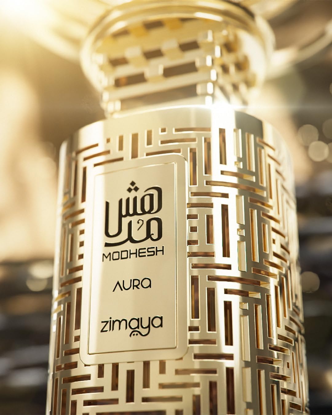 Gold-patterned perfume bottle with 'Modhesh Aura' and 'Zimaya' branding on a blurred background