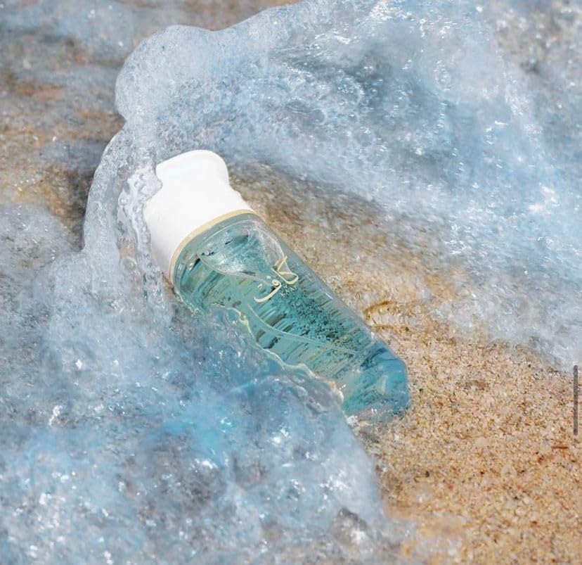 Ahmed Al Maghribi Kaaf bottle with a white cap on a beach with waves