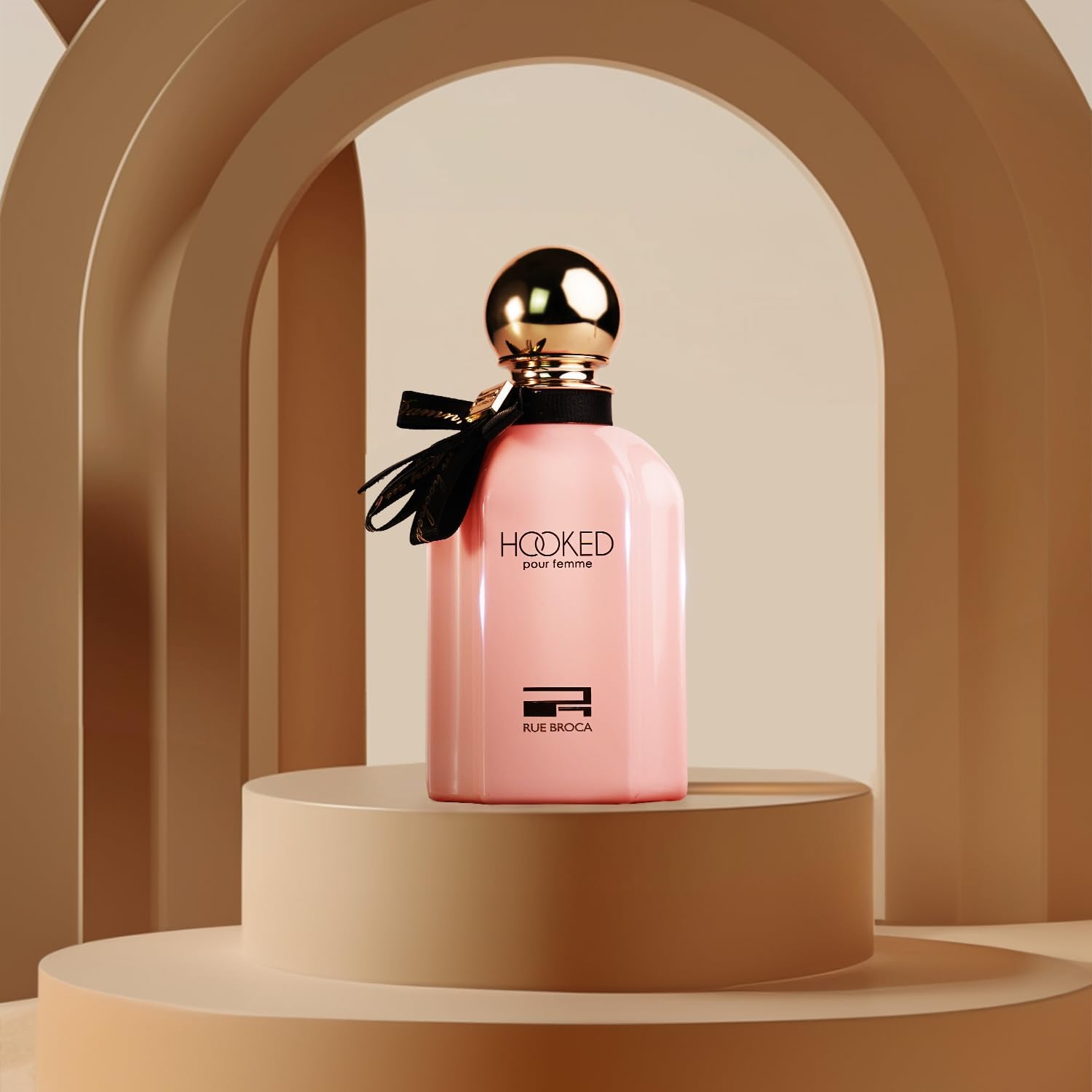 Rue broca Hooked Pour Femme Pink perfume bottle with gold cap on a beige platform against a beige archway