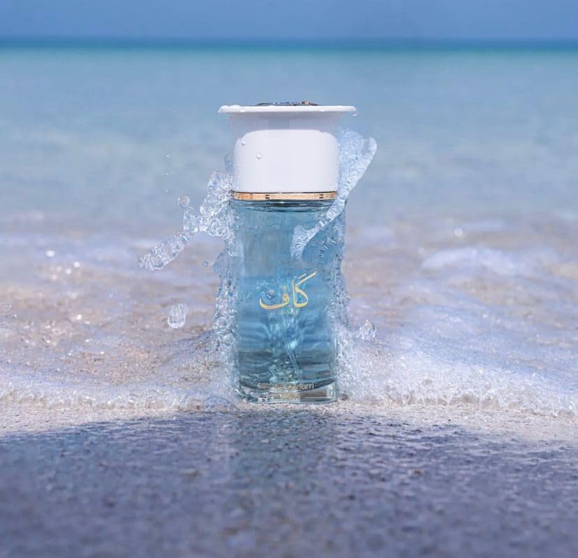 Ahmed Al Maghribi Kaaf Blue bottle with white cap on a beach with ocean in the background