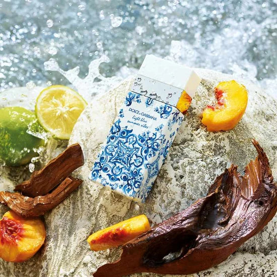 Dolce & Gabbana light blue eau de toilette with fruits and chocolate on a stone surface with water splashing around.