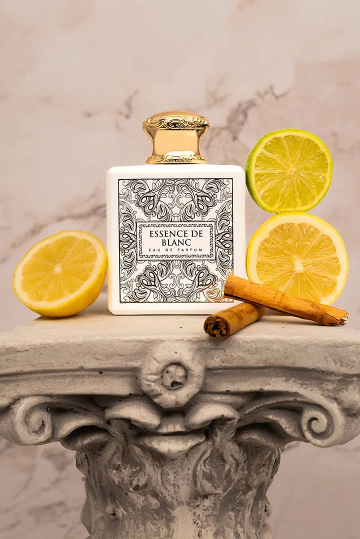 Perfume bottle labeled 'Essence de Blanc' with lemon slices and cinnamon sticks on a decorative stone surface.