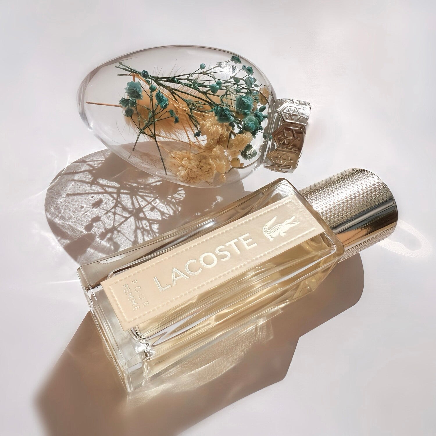 Lacoste perfume bottle with a decorative cover featuring dried flowers on a light background