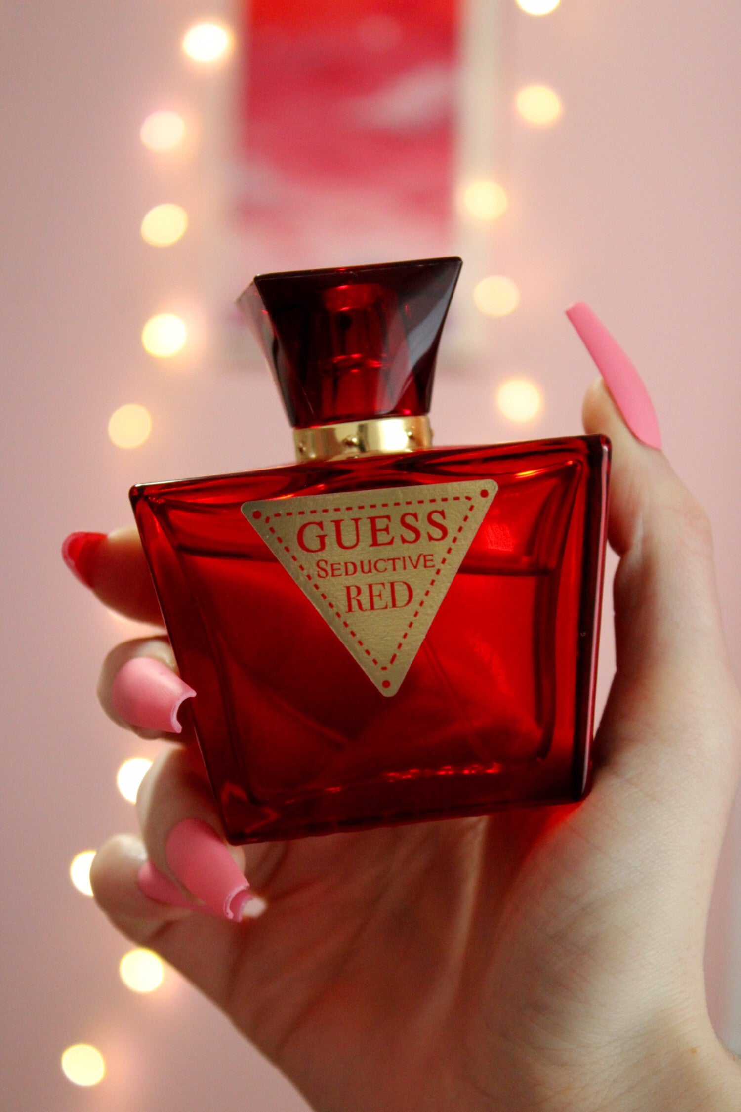 Red Guess perfume bottle held by a hand with a blurred light background