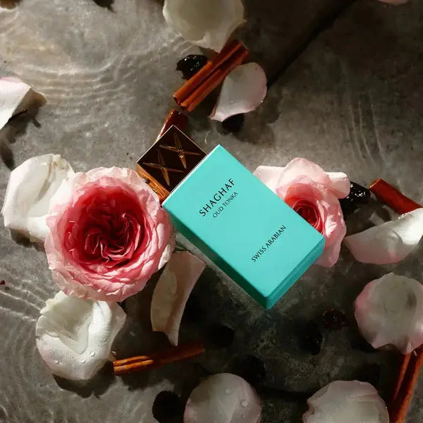 Shaghaf perfume box surrounded by pink roses and cinnamon sticks on a textured surface