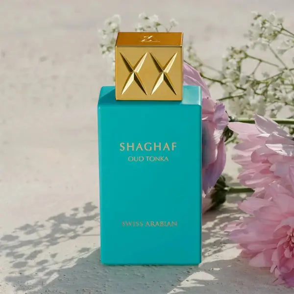Shaghaf Oud Tonka perfume bottle with a gold cap on a light background with flowers.
