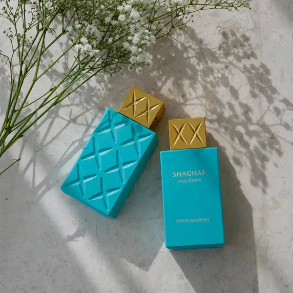 Two turquoise perfume bottles with gold caps on a textured surface with white flowers.