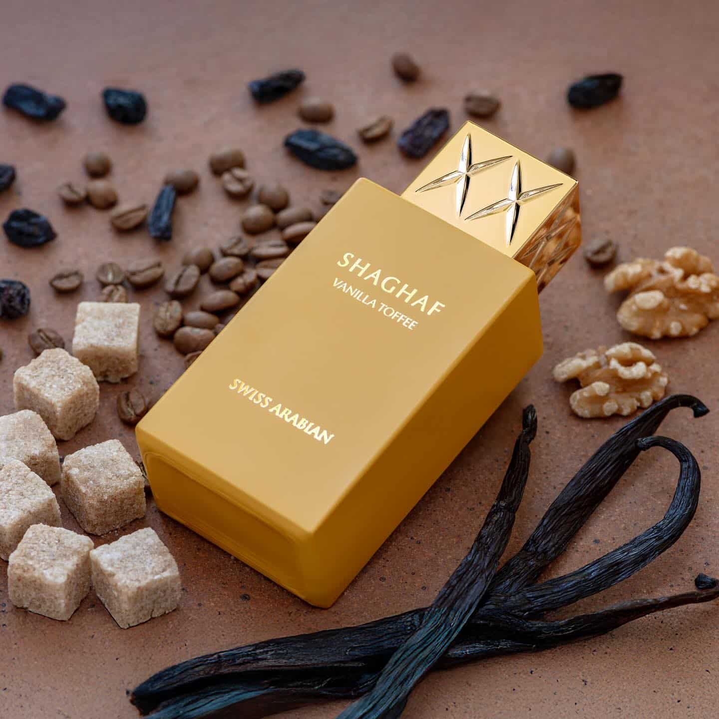 Shaghaf Vanilla Toffee Yellow perfume bottle with vanilla toffee fragrance surrounded by vanilla beans, sugar cubes, and nuts on a brown background.