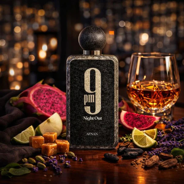Perfume bottle labeled '9pm Night Out' by Afnan with a glass of whiskey and fruit on a wooden surface.