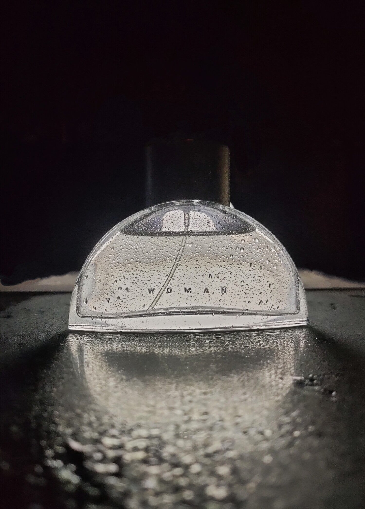 Metallic object with 'WOMAN' engraved on it, reflecting light on a dark background