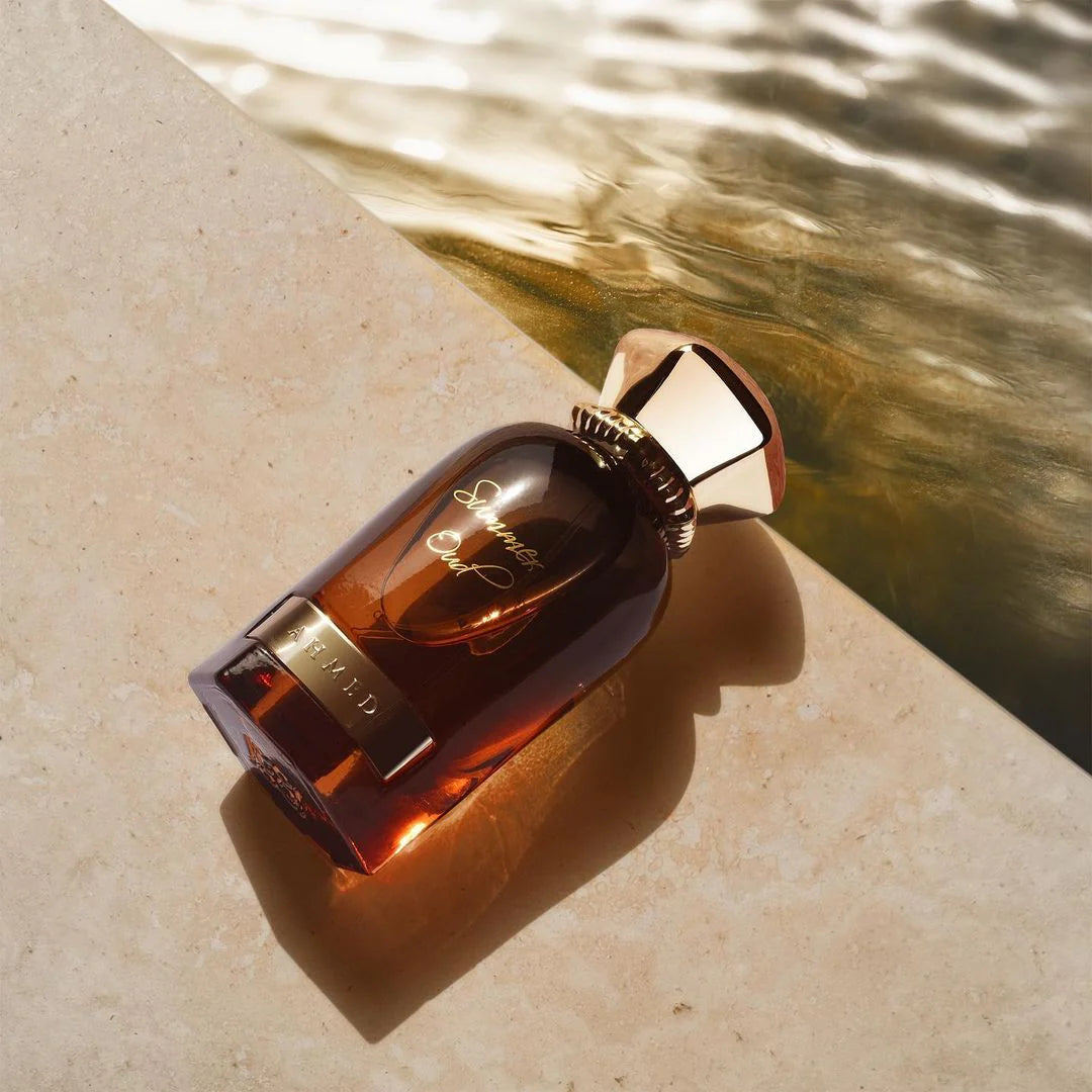 Ahmed Al Maghribi Summer Oud Brown perfume bottle with gold cap on a textured surface with water reflection