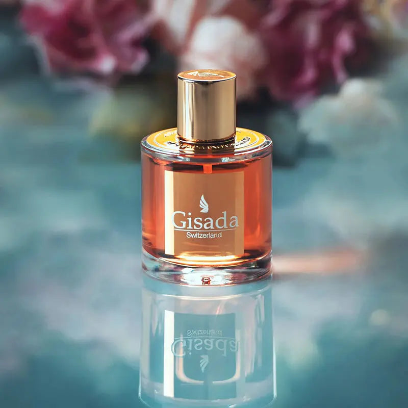 Gisada perfume bottle with a gold cap on a reflective surface with a blurred floral background