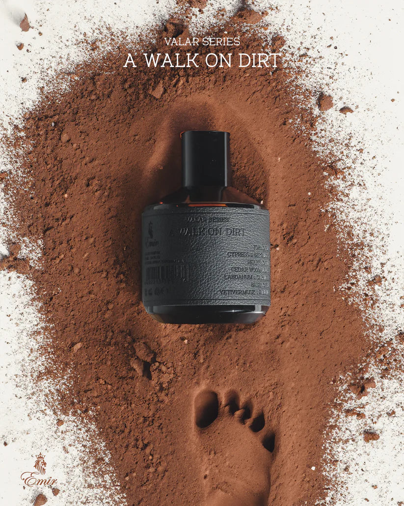 Black bottle of perfume on a bed of dirt with footprints, labeled 'A Walk on Dirt' from the Valar Series.