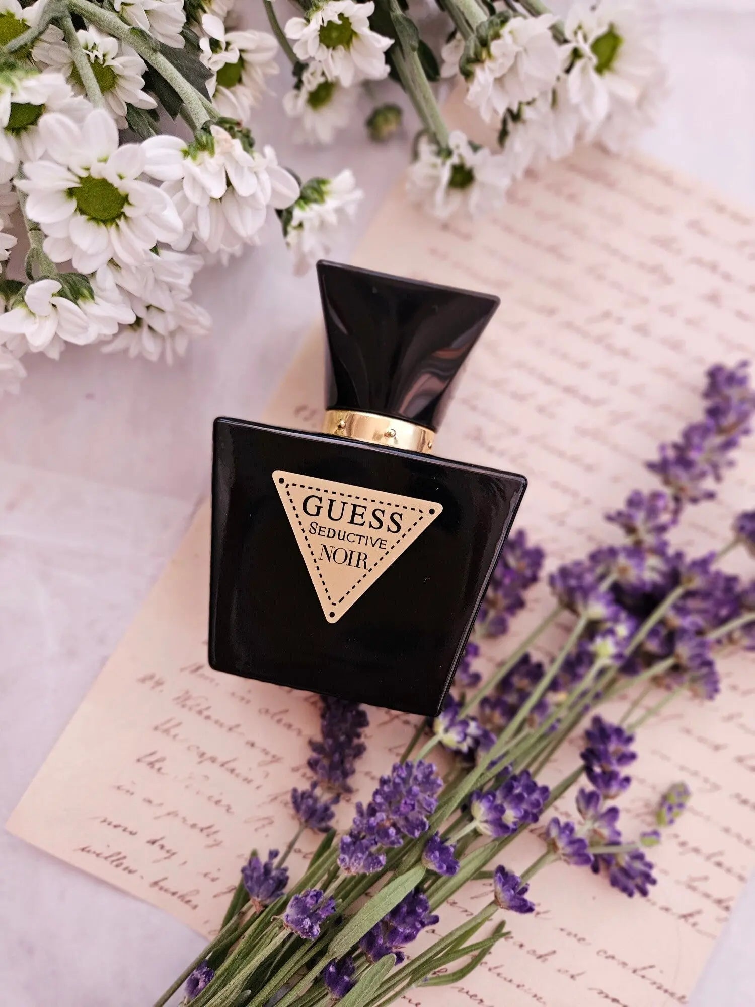 Guess perfume bottle on a surface with flowers and paper