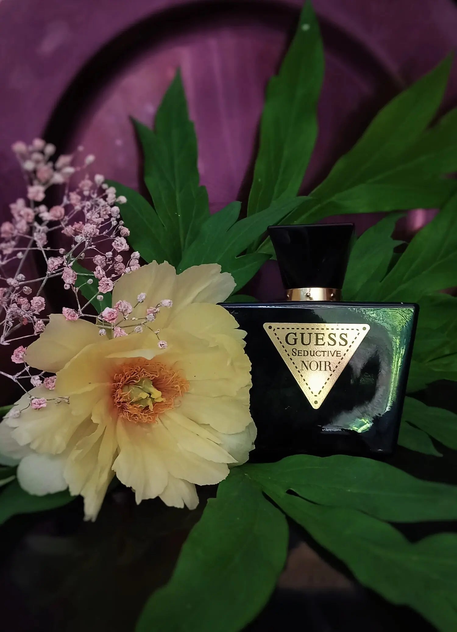 Guess perfume bottle with a yellow flower and green leaves on a purple background