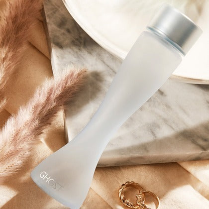 White bottle with silver cap on a marble surface with pampas grass and a ring.