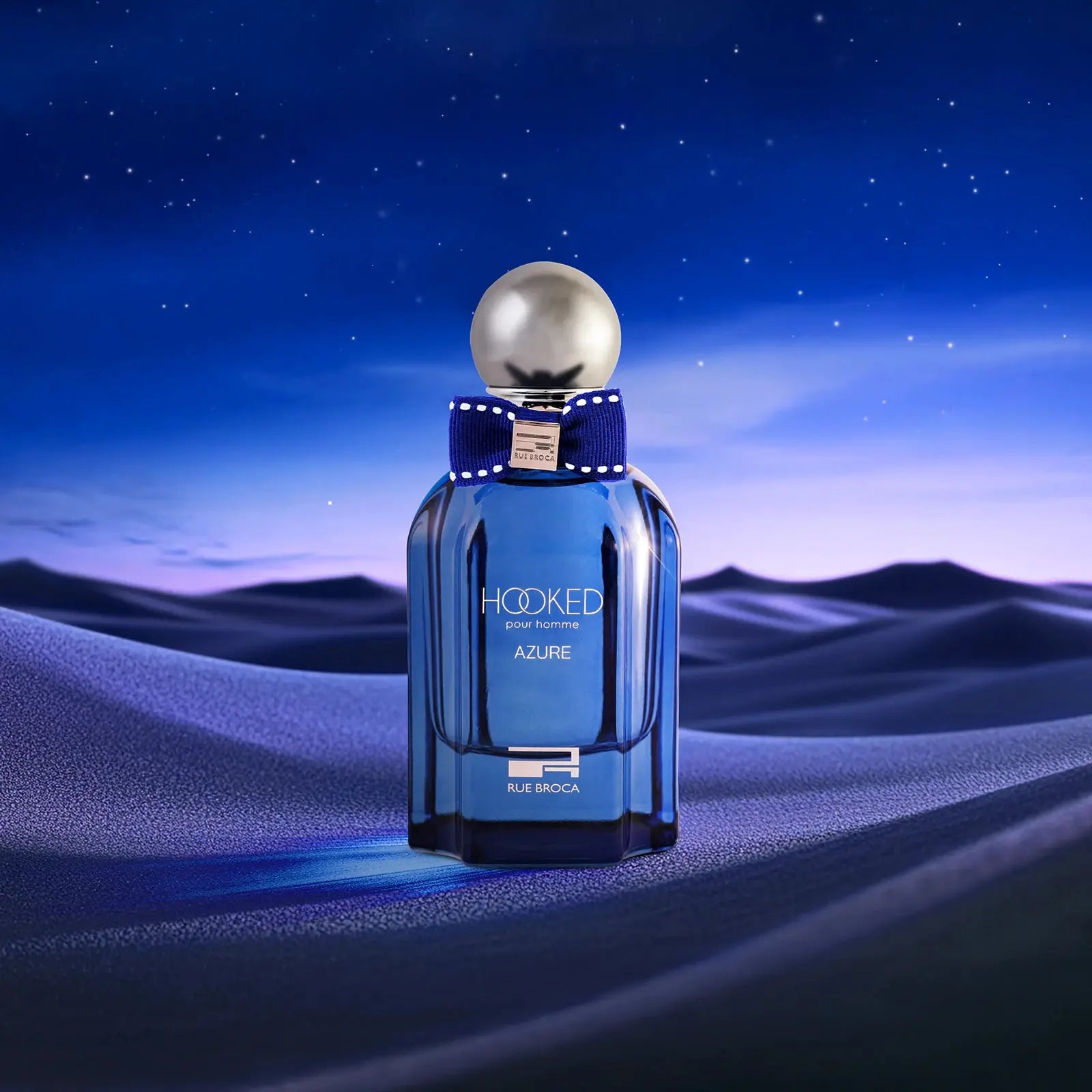 Blue perfume bottle labeled 'Hooked Azure' on a desert landscape with a starry sky.