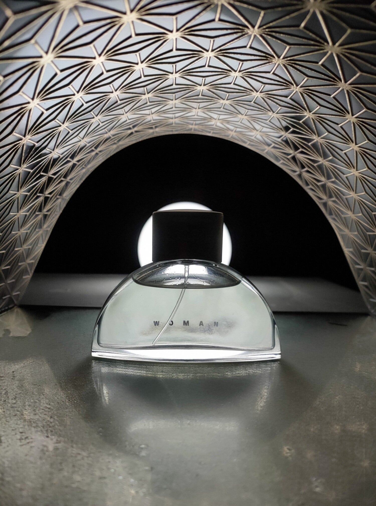 Perfume bottle on a reflective surface with a geometric wall in the background