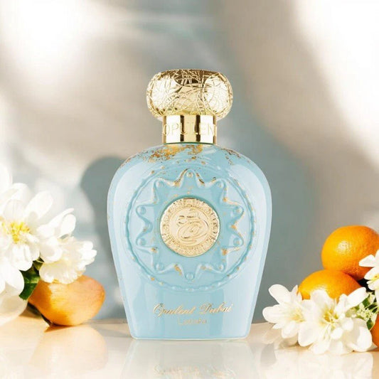 Lattafa Opulent Dubai Blue perfume bottle with gold accents on a light background with flowers and oranges.
