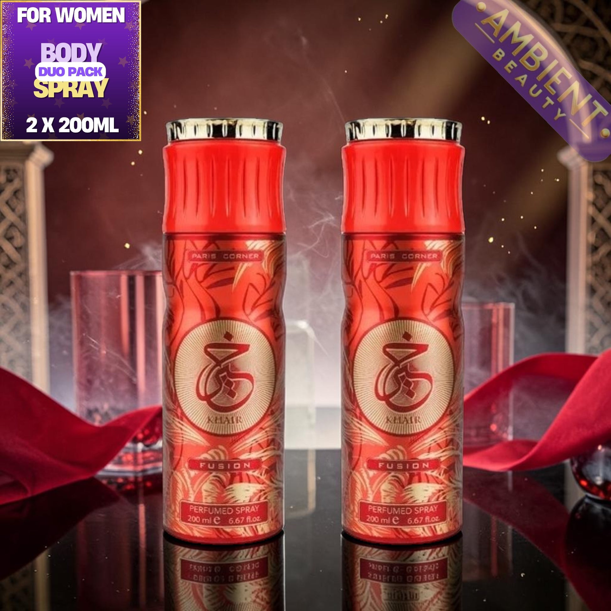 Two red and gold perfume spray bottles labeled 'Khair' and 'FUSION' on a reflective dark surface, with red fabric, glassware.