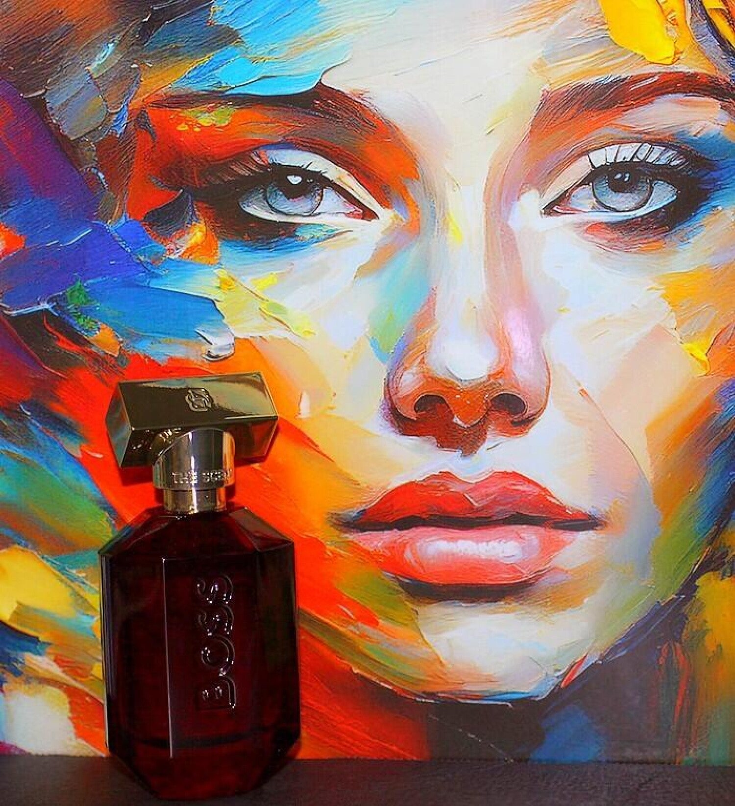 Colorful abstract painting of a face with a Boss perfume bottle in front.