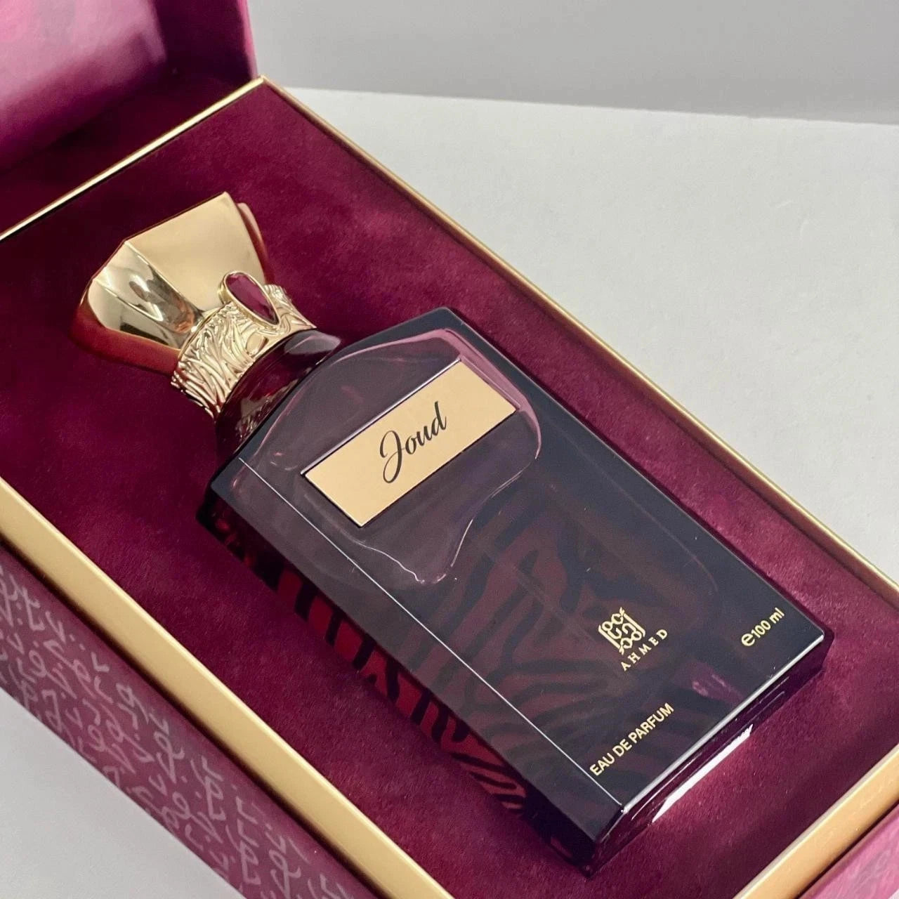 Ahmed Al Maghribi Joud Perfume bottle with gold cap and label on a maroon background