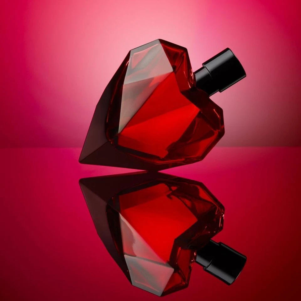 Diesel Red perfume bottle on a reflective surface with a pink gradient background