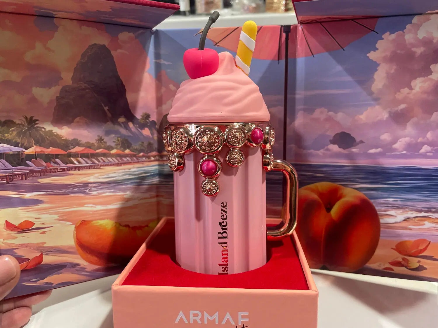 Pink milkshake-shaped mug with decorative elements in a box, beach scene in the background